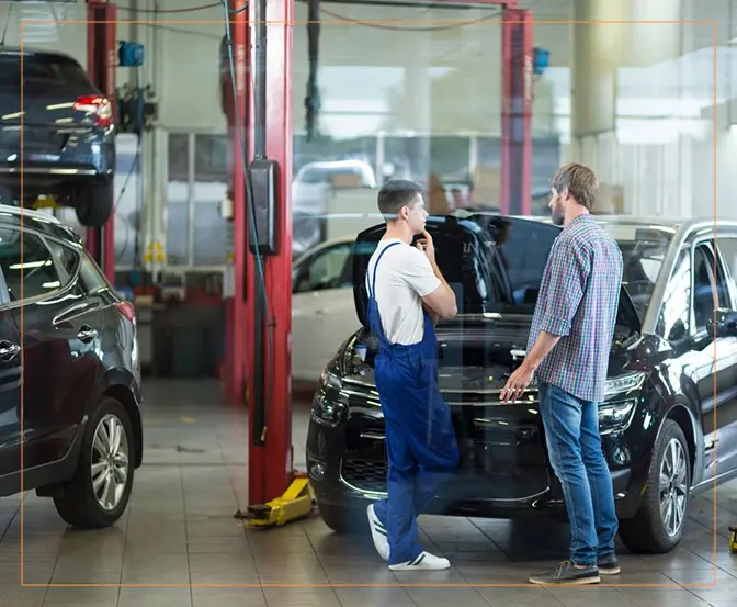 Two men standing next to a car in an automotive services garage.